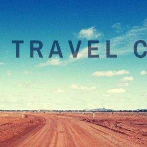 Image contains a photo of a long dirt road heading to the horizon. The sky above is mostly clear and blue with a few small white clouds. In the foreground, there is black text that says "Global Travel Channel".