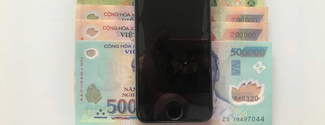 Image contains a photo of an iPhone 5s on top of a number of bills in Vietnamese currency.