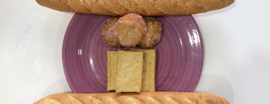 Image contains a photo of a purple plate with blocks of tofu and sugared balls on it. On opposite sides of the plate, there are two baguettes.