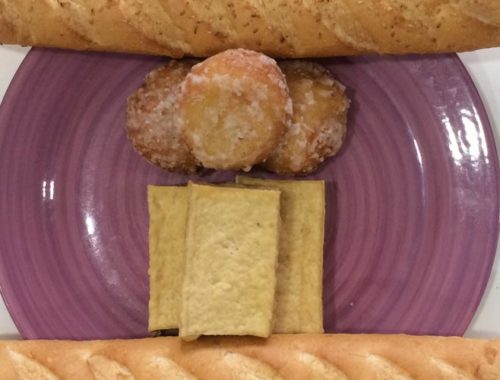 Image contains a photo of a purple plate with blocks of tofu and sugared balls on it. On opposite sides of the plate, there are two baguettes.