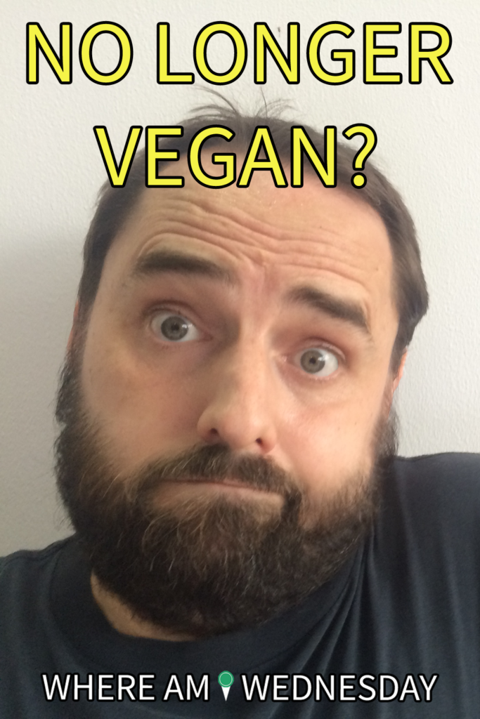 Image contains a photo of a bearded man with a questioning look on his face and his shoulder raised. Above the man, there is yellow text that says "No Longer Vegan?" and below him there is white text that says "Where Am I Wednesday".