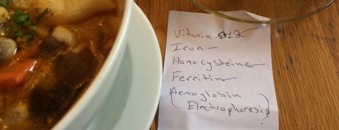 Image contains a photo of a white bowl of soup and noodles on the left, a glass cup of tea in the top right-hand corner, and a paper note in the bottom right-hand. On the note, there is handwriting that says "Vitamin B12, iron, homocysteine, ferritin, and hemoglobin electrophoresis."