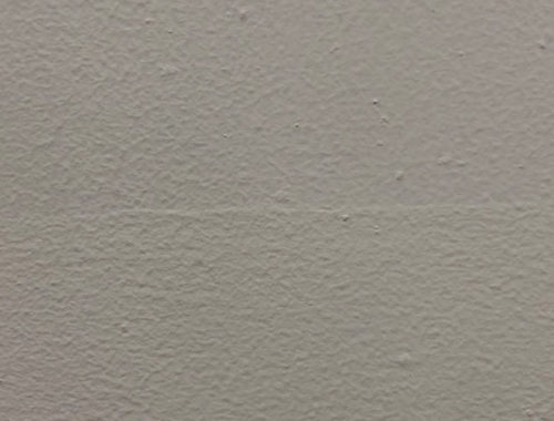 Image contains a photo of a painted white wall with small bumps and a thin line going across the middle.